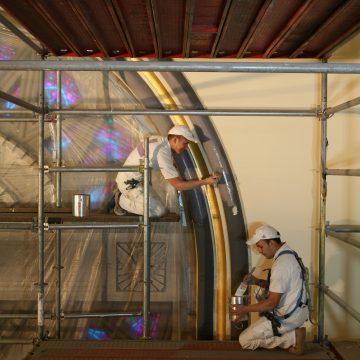 Two men painting in a church on scaffolding
