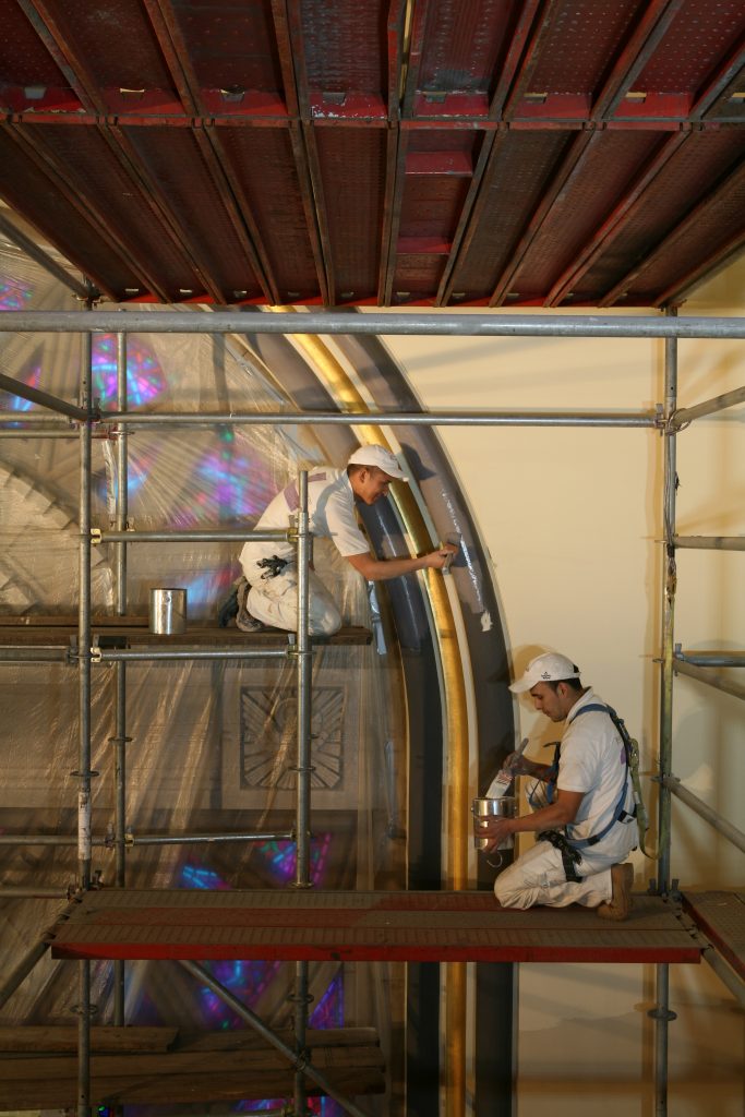 Two men painting in a church on scaffolding