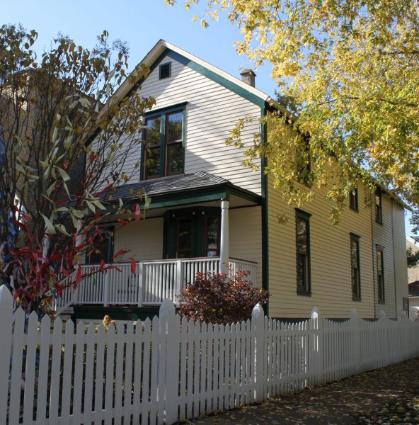 Walt Disney birthplace home after restoration showing cream wood clapboard siding, green trim, restored front porch, and white picket fence in Chicago