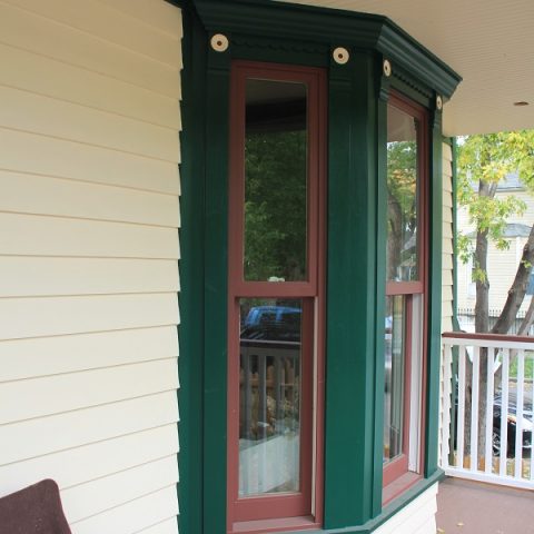 Restored bay window with green and red historic trim and cream clapboard siding on the Walt Disney birthplace home porch in Chicago