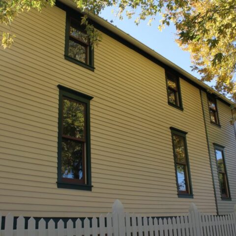 Restored yellow wood clapboard siding with green window trim on the side elevation of the Walt Disney birthplace home in Chicago